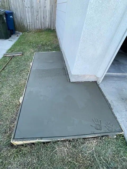 Concrete trash-can pad with a dark metal enclosure beside a house